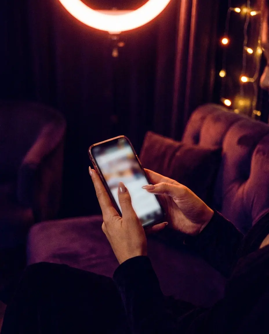 Hands holding a phone in a warm evening interior, the screen glowing softly